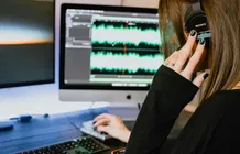 Una mujer con auriculares mira una pantalla con variaciones de audio.